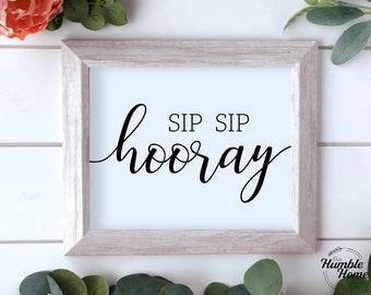 May include: A white framed print with black calligraphy that reads "Sip Sip Hooray".
