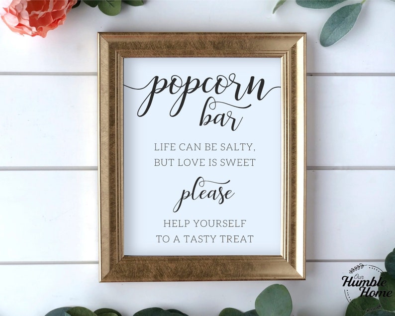 Op de afbeelding: Een gouden lijst met de tekst "popcorn bar" in zwarte cursieve letters. Het bord bevat ook de tekst "Life can be salty, but love is sweet. Please help yourself to a tasty treat." in zwarte letters.