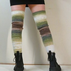 May include: Knee-high leg warmers in shades of green, brown, and white. The striped pattern transitions from white at the top to green and brown, with black boots visible at the bottom. The leg warmers are made of a soft, knitted material.