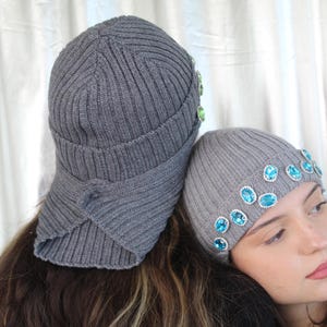 May include: Two gray knit hats with blue and green embellishments. One hat is folded down and the other is worn on a person's head.