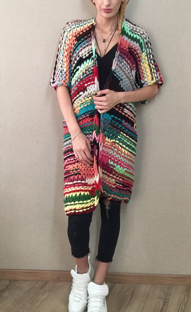May include: A long, colourful, striped cardigan with a loose fit and short sleeves. The cardigan is made of chunky yarn and has a casual, bohemian style.