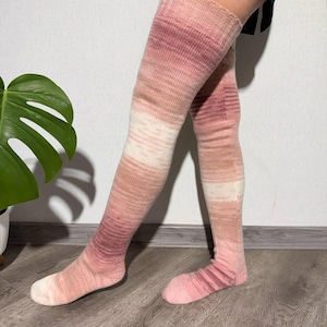 Peut inclure: Chaussettes hautes aux genoux dans des tons roses et blancs. Les chaussettes présentent une texture côtelée et un motif de couleur dégradé, passant d'un rose foncé en haut à un rose plus clair au pied. Les chaussettes sont portées sur les jambes.