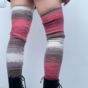May include: A pair of long, striped knee-high socks in shades of pink, brown, and white. The socks are worn over black boots.