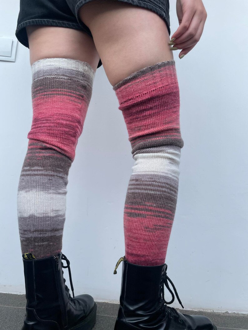 May include: A pair of long, striped knee-high socks in shades of pink, brown, and white. The socks are worn over black boots.