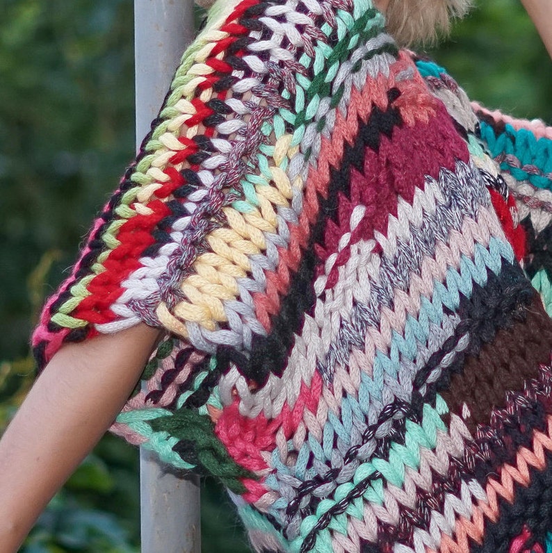 May include: A colourful crocheted top featuring a mix of red, green, blue and brown hues. The top is crafted from chunky yarn and has a loose, relaxed fit.