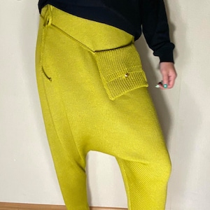 May include: Yellow knitted pants with a large pocket on the right side. The pants have a unique, loose fit.