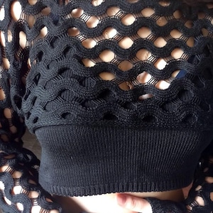 Könnte beinhalten: Schwarzes, langärmliges Crop-Top mit Häkelmuster. Das Top hat einen weiten Ausschnitt und eine figurbetonte Silhouette.