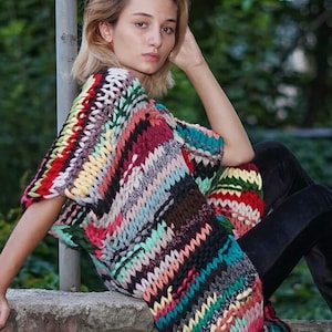 May include: A colourful striped crochet top with a loose fit and short sleeves. The top is made with a chunky yarn and has a variety of colours, including red, blue, green, yellow, and pink.