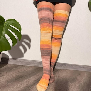 May include: Knee-high socks in a gradient of colors, including orange, yellow, pink, and brown. The socks are made of a knitted material and are designed to be worn over the knee. The socks have a ribbed cuff at the top.