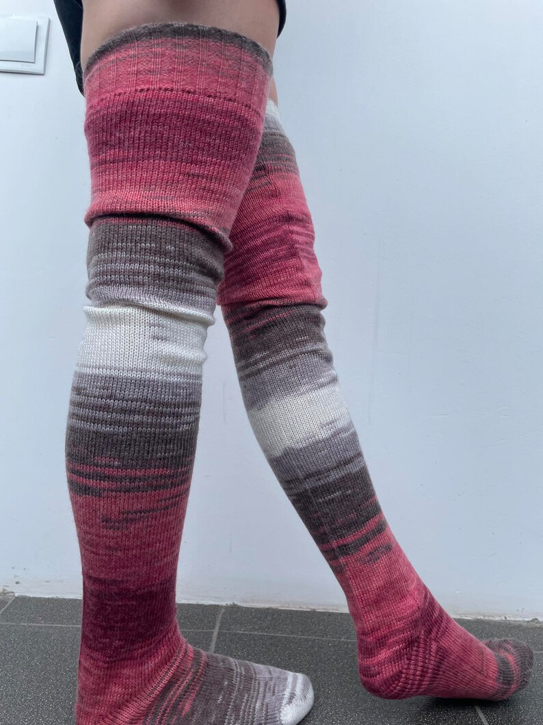 May include: A pair of long, knitted thigh-high socks with a pink, white, and brown ombre pattern.