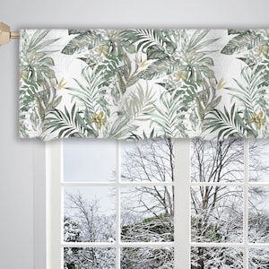 May include: A white valance with a green and yellow tropical leaf pattern. The valance is hung on a window with a view of a snowy winter landscape.