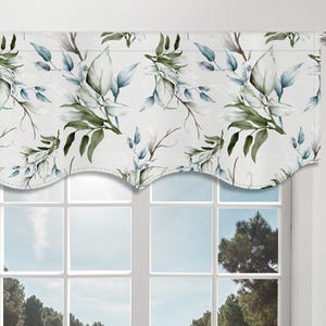 May include: A white window valance with a floral pattern of green and blue leaves and branches. The valance is mounted on a silver rod above a white window. The window overlooks a green field and trees under a blue sky.