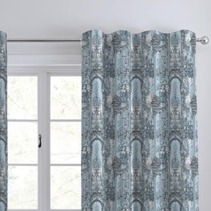 May include: Two blue and gray patterned curtains hanging in front of a window. The curtains feature a repeating design of architectural elements and floral accents. The curtains are made of a thick fabric and are likely used for privacy and light control.
