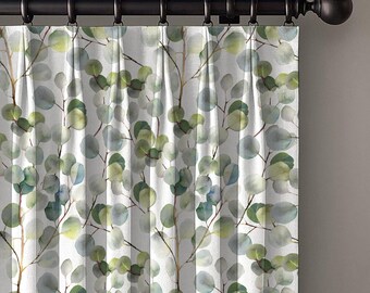 May include: A pair of white curtains with a watercolor eucalyptus leaf pattern in shades of green and blue. The curtains are hanging from a dark brown metal rod with decorative finials.