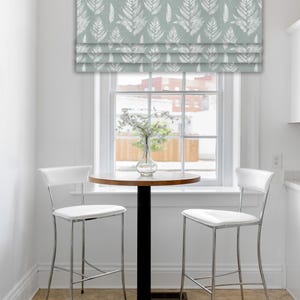 May include: A window treatment with a fern pattern in white on a light blue background. The window is above a small round table with two white chairs. The room has a neutral color palette.