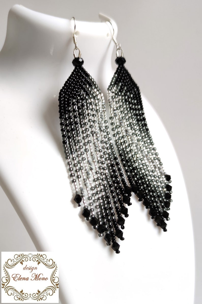 May include: A pair of long, black and silver beaded earrings with a graduated ombre effect. The earrings are made with small, faceted beads and have a teardrop shape.