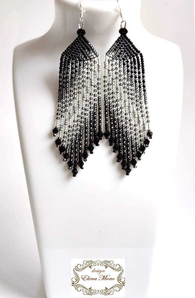 May include: Long black and silver beaded earrings with a graduated ombre effect. The earrings are made with small seed beads and have a teardrop shape.