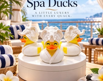 May include: Three yellow rubber ducks wearing white bathrobes and white towel head wraps. The text Spa Ducks A LITTLE LUXURY WITH EVERY QUACK is visible above the ducks. The ducks are positioned on a white circular platform.
