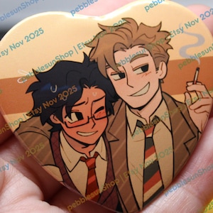 May include: Heart-shaped button with an illustration of two men in suits, one smoking. The button has a tan background with the text "pebblesunShop | Etsy Nov 2025" repeated around the edges. The men are smiling and wearing ties.