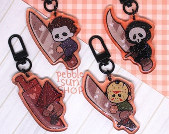 May include: Four colorful keychains featuring cartoon characters holding knives. Each keychain has a black metal zipper pull. The characters are a masked killer, a grim reaper, a red-hooded figure, and a masked man.