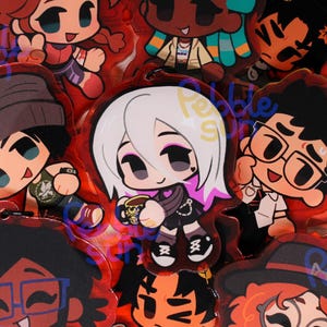 Może przedstawiać: Kolekcja czerwonych akrylowych breloków do kluczy z postaciami z kreskówek o różnych fryzurach i strojach. Każdy brelok ma czarny łańcuszek i czerwoną obwódkę. Postacie mają różne odcienie skóry i wyrazy twarzy.