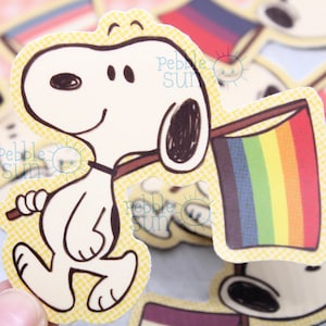 May include: A set of colourful cartoon dog stickers with a rainbow flag, a yellow, purple and black flag, and a red, white and blue flag. The stickers are on a checkered background.