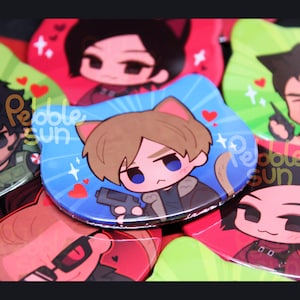 May include: A collection of colorful, cat-eared character badges. The central badge features a cartoon character with brown hair, holding a gun, set against a blue background with hearts. The badges are from Pebble Sun.