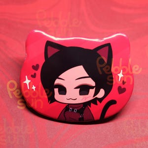 May include: A red, cat-shaped pin featuring a cartoon character with black hair and cat ears. The character is wearing a red outfit and surrounded by hearts and stars. The pin has a glossy finish.