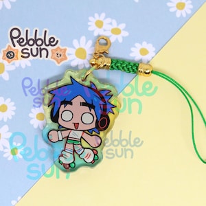 May include: A clear acrylic charm featuring a cartoon character with blue hair, headphones, and roller skates. The charm has a green border and is attached to a green cord with a gold clasp. The background has a daisy pattern and the text "Pebble Sun".