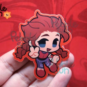 May include: A sticker featuring a cartoon character with red hair in pigtails, wearing a red and purple outfit, giving a peace sign. The sticker has a red border and the text "Pebble Sun" in the upper left corner.