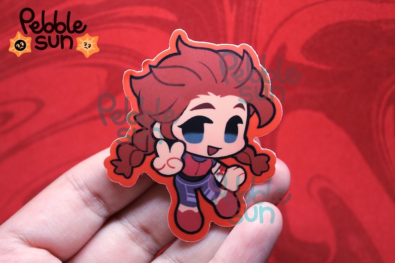 May include: A sticker featuring a cartoon character with red hair in pigtails, wearing a red and purple outfit, giving a peace sign. The sticker has a red border and the text "Pebble Sun" in the upper left corner.