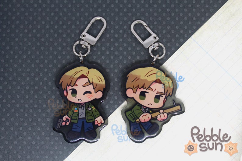 May include: Two cartoon character keychains with silver key rings. The characters are male with brown hair and are wearing different outfits. One character is holding a gun and the other is holding a knife.