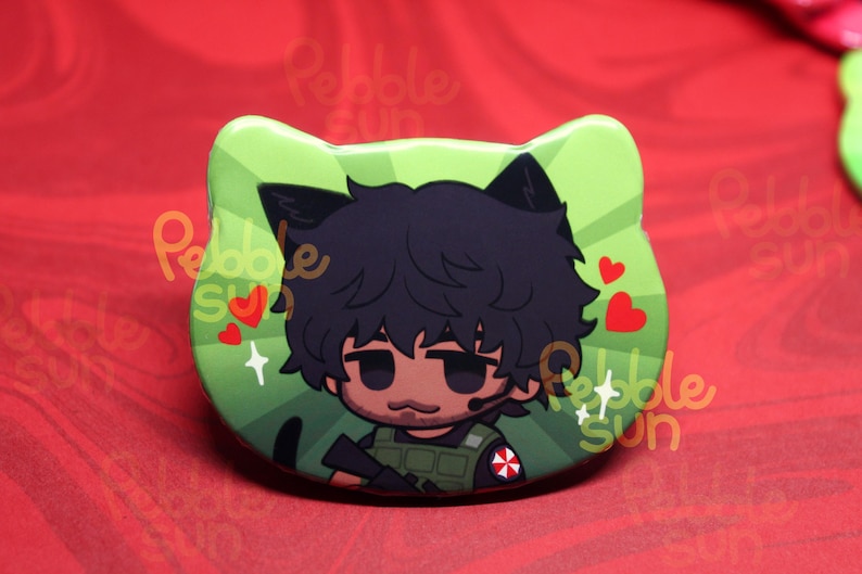 May include: A green cat-shaped button featuring a cartoon character with black hair and cat ears. The character wears a military vest and has a headset. Red hearts and the text "Pebble Sun" are also visible.