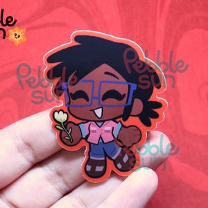 May include: A sticker featuring a cartoon character with dark skin, black hair, and blue glasses, holding a white flower. The character wears a pink vest, blue jeans, and brown sandals. The sticker has the text "Pebble Sun" and a sun logo.