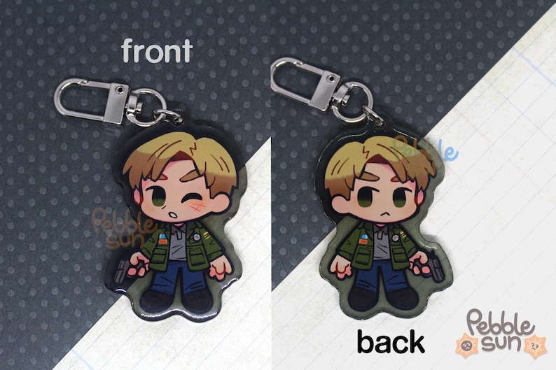 May include: A keychain featuring a cartoon character with brown hair, wearing a green jacket and blue jeans. The keychain is made of clear acrylic and has a silver metal ring.