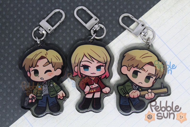 May include: Three cartoon character keychains with silver key rings. The characters are a woman with pink hair wearing a red top and a black skirt, a man with brown hair wearing a green jacket, and a man with brown hair wearing a green jacket and holding a wooden stick.