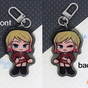 May include: A keychain featuring a cartoon character with blonde hair, wearing a red shirt, a black skirt, and black boots. The keychain is made of clear acrylic and has a silver metal ring.