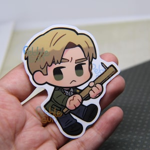 May include: A sticker featuring a cartoon character with blonde hair, wearing a green jacket and black pants, holding a wooden weapon. The character has a serious expression and is outlined in black.