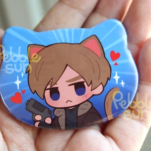 May include: A blue cat-shaped button featuring a cartoon character with brown hair, cat ears, and a serious expression, holding a gun. The design includes hearts and starbursts. The text "Pebble Sun" is visible.