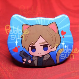 May include: A blue, cat-shaped button featuring a cartoon character with brown hair, holding a gun. The background is blue with white sparkles and red hearts. The button has the text "Pebble Sun".