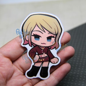 May include: A die-cut sticker featuring a cartoon character with blonde hair and pink highlights. The character wears a maroon top, a patterned skirt, and black boots. The sticker is held in a hand.