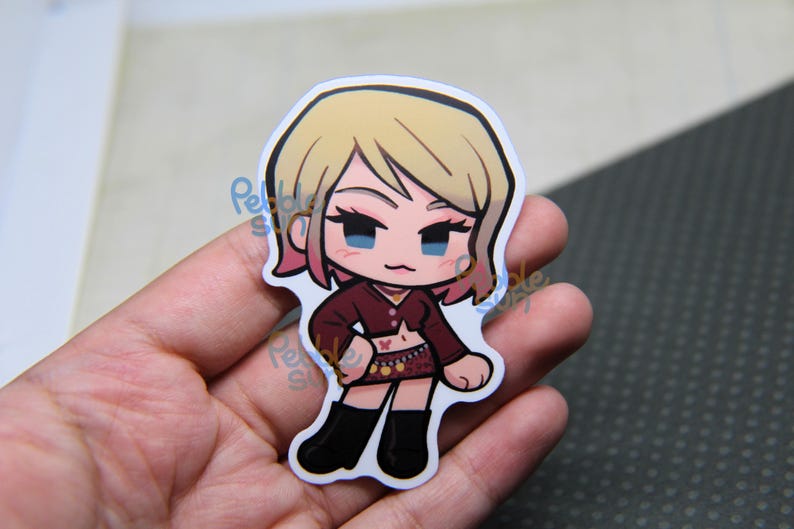 May include: A die-cut sticker featuring a cartoon character with blonde hair and pink highlights. The character wears a maroon top, a patterned skirt, and black boots. The sticker is held in a hand.