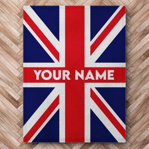 Pode incluir: Um cobertor azul, vermelho e branco com o design da bandeira da Union Jack. O texto "YOUR NAME" é impresso em branco no cobertor.