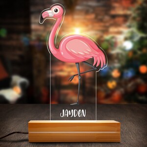 May include: A pink flamingo night light with a wooden base. The light has the name "Jayden" written on it.
