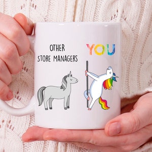May include: White ceramic mug with a unicorn illustration and the text "Other Store Managers" and "You". The unicorn representing "You" is holding a pole and has a rainbow mane and tail. The other unicorn is gray.