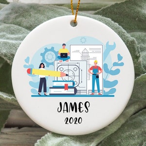 May include: White ceramic ornament with a blue and white illustration of three people working on a blueprint. The text "JAMES 2020" is printed below the illustration.
