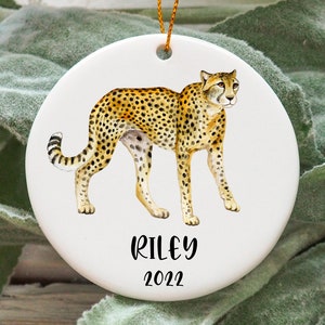 May include: White ceramic bauble featuring a watercolour illustration of a cheetah and the text "Riley 2022".