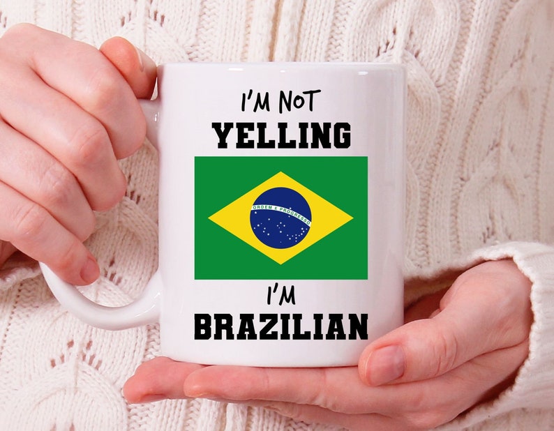 Op de afbeelding: Witte keramische mok met een zwart-gele Braziliaanse vlag en de tekst "Ik schreeuw niet, ik ben Braziliaans".