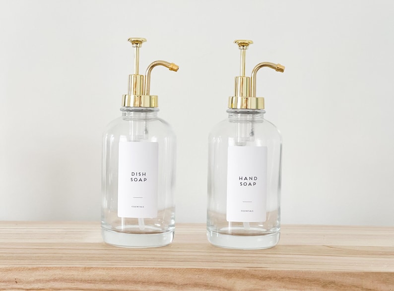 May include: Two clear glass soap dispensers with gold pumps and labels that read "Dish Soap" and "Hand Soap".