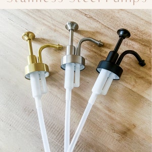 May include: Three soap pumps with different finishes: gold, silver, and black. The pumps have clear plastic tubes.